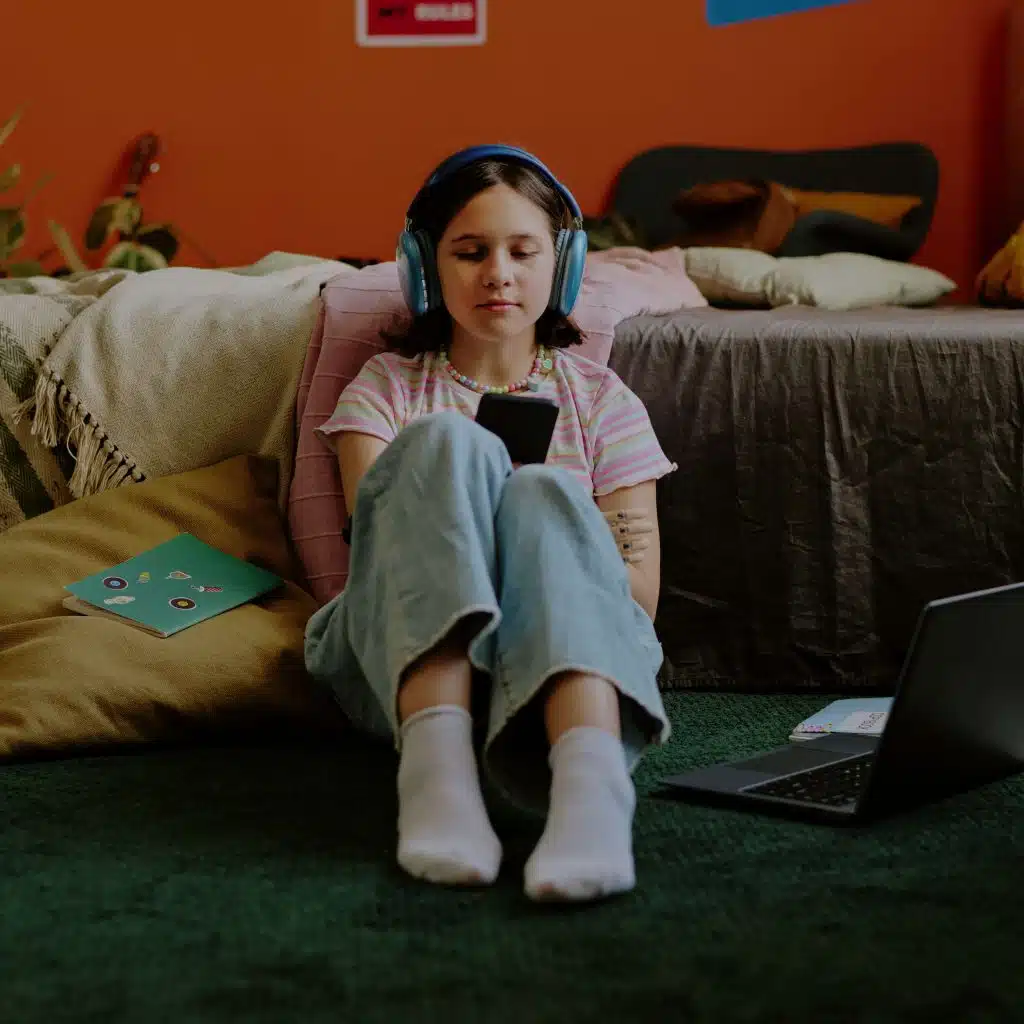 Joven niña con auriculares y teléfono móvil, participación en actividades digitales y de entretenimiento, en un ambiente familiar y moderno.