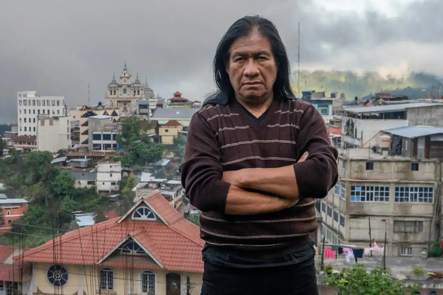 Multimedia journalist with urban background, cityscape, mountains, cloudy sky, resident of urban area, documentary photography, cultural and social themes, featuring a person outdoors. – SoyMigrante.com REVISTA
