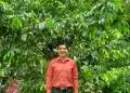Amplio árbol de hoja perenne con un hombre sonriendo en medio de la naturaleza, símbolo de crecimiento y sostenibilidad para artículos de agricultura y medio ambiente en SoyMigrante.com REVISTA.