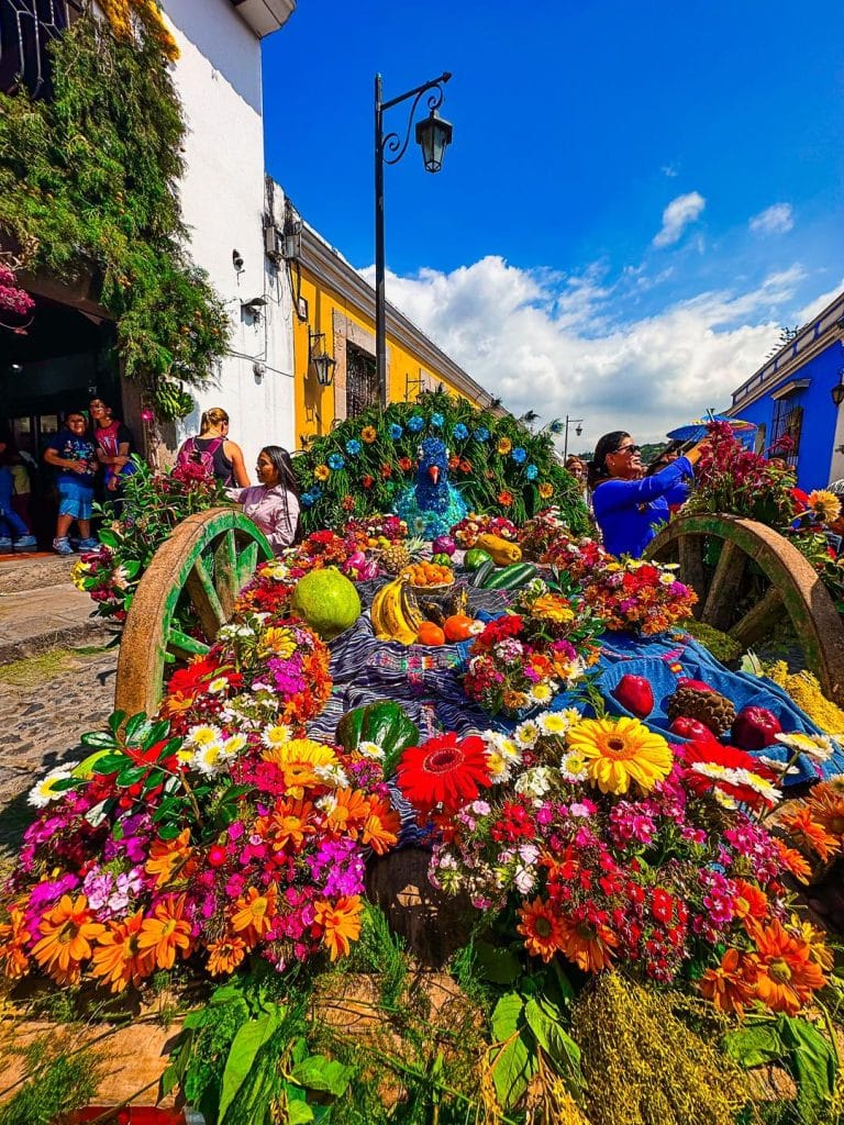 Colorido altar de Día de Muertos decorado con flores, frutas y calaveras en una celebración tradicional mexicana en un pueblo con calles pintadas en colores vivos.
