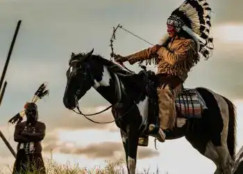 Guerrero indígena montado a caballo con plumas tradicionales en ceremonia cultural en la naturaleza.