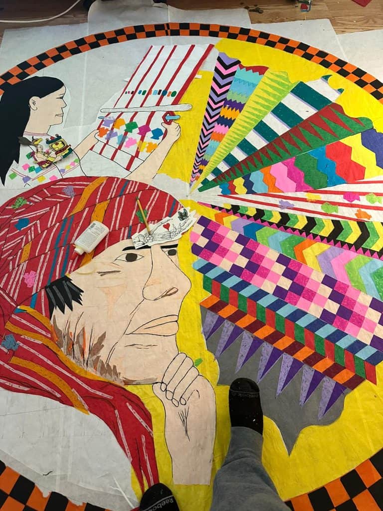 Colorido mural de arte indígena y cultura popular en proceso de creación, resaltando patrones tradicionales y modernos en un trabajo artístico colaborativo.