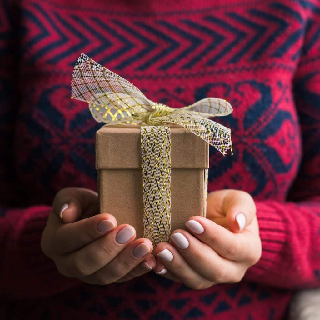 Regalo envuelto con cinta decorativa en manos, símbolo de celebración y solidaridad en la comunidad migrant, destacando la importancia de la integración y la cultura en la revista SoyMigrante.com REVISTA.