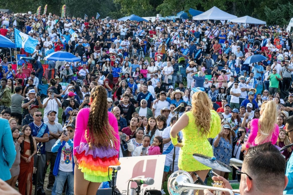Celebración de la cultura y la identidad migrante en un evento masivo con espectadores de diferentes edades, resaltando la comunidad y festividades de los migrantes latinoamericanos.