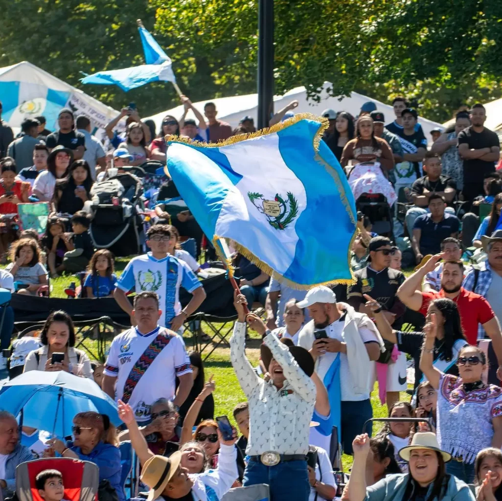 Banderas y símbolos de Guatemala en una celebración cultural llena de inmigrantes y comunidad en un parque, promoviendo la identidad y orgullo guatemalteco.