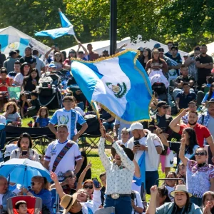 Banderas y símbolos de Guatemala en una celebración cultural llena de inmigrantes y comunidad en un parque, promoviendo la identidad y orgullo guatemalteco.