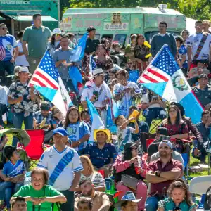 Celebración de migrantes en un evento cultural, con banderas de Estados Unidos, Guatemala, y Cuba, mostrando orgullo y comunidad en un ambiente festivo y multicultural.