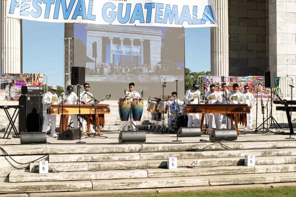 Festival Guatemala en el escenario con músicos tocando instrumentos tradicionales durante un evento cultural al aire libre.