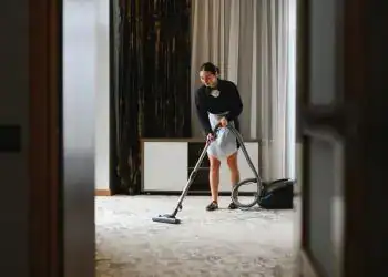 Nana limpiando una habitación con aspiradora en un hotel moderno, mostrando servicios de limpieza y cuidado del hogar para migrantes en el contexto de #SoyMigrante.