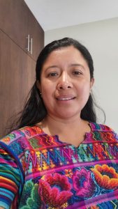 Mujer sonriendo con vestimenta tradicional colorida, en entorno moderno, representando diversidad cultural en México. – SoyMigrante.com REVISTA