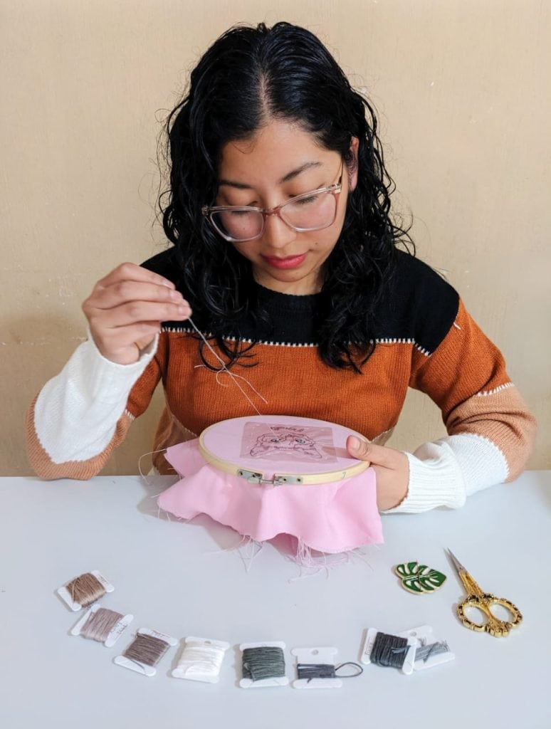A mujer cosiendo bordado en bastidor, proyecto de arte y manualidades, técnica de costura creativa y habilidades tradicionales, en un ambiente de trabajo artesanal.