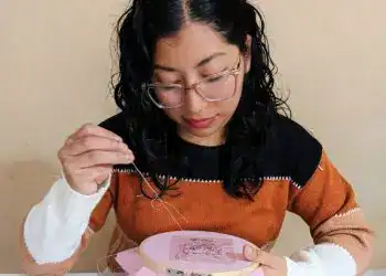 A mujer cosiendo bordado en bastidor, proyecto de arte y manualidades, técnica de costura creativa y habilidades tradicionales, en un ambiente de trabajo artesanal.