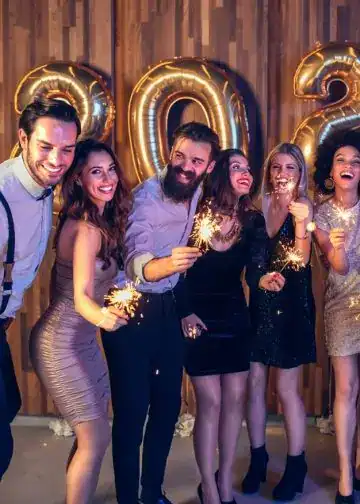 Celebrities celebrando con bengalas en una fiesta de fin de año 2022, decorada con globos dorados en forma de números 2023, mostrando alegría y unión en la celebración. – SoyMigrante.com REVISTA