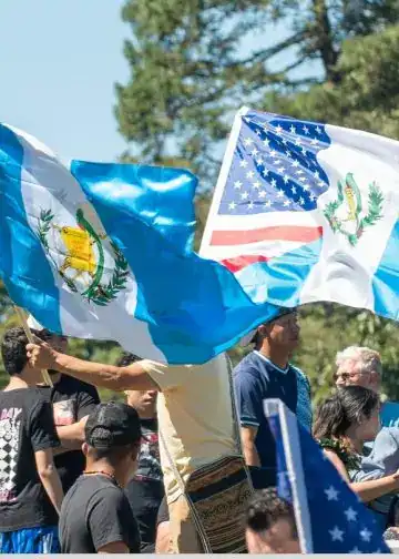 Guatemaltecos y estadounidenses participan en una manifestación con banderas de Guatemala y Estados Unidos en un parque al aire libre. – SoyMigrante.com REVISTA