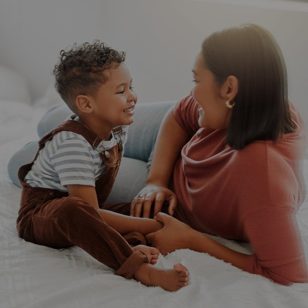 Niño sonriendo con madre en ambiente hogareño, destacando la importancia de la familia en la comunidad de migrantes. – SoyMigrante.com REVISTA