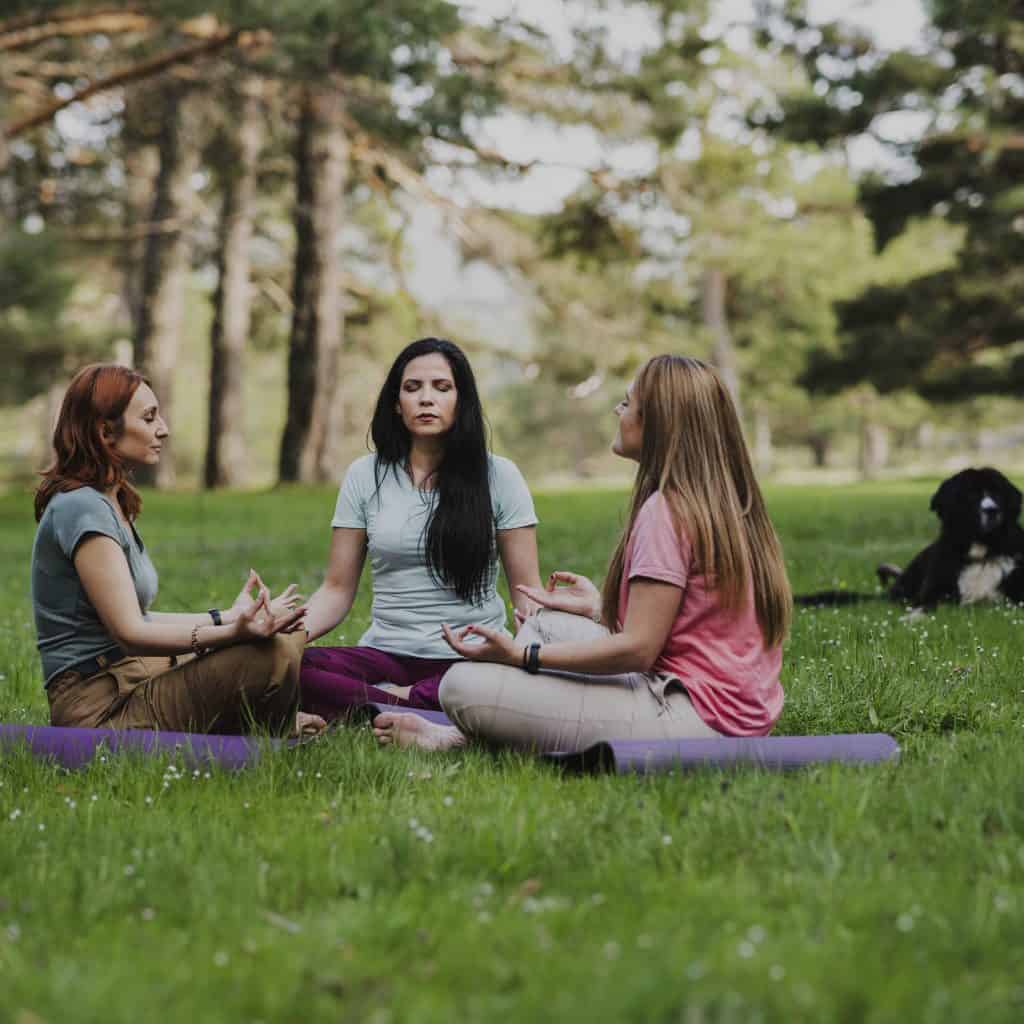 Meditación en grupo de mujeres en un parque, practicando yoga y mindfulness, promoviendo bienestar, salud mental y conexión con la naturaleza. Concepto de relajación y equilibrio emocional. – SoyMigrante.com REVISTA