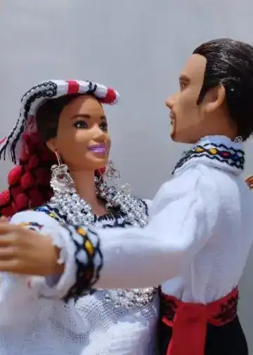 Diversidad cultural en celebración, figura de muñecos de pareja con trajes tradicionales, representación artística de migrantes en la Revista SoyMigrante, enfatizando la integración y cultura latinoamericana.