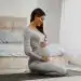 Mujer embarazada haciendo yoga, practicando meditación en casa, ejercicio prenatal para futuras madres, bienestar y salud durante el embarazo, revista SoyMigrante.com.