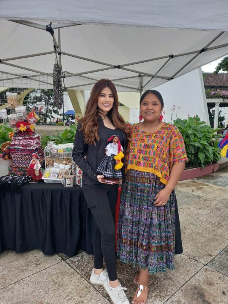 Artesanías y cultura mexicana en feria con mujeres indígenas vestidas con ropa tradicional y accesorios coloridos en evento cultural. – SoyMigrante.com REVISTA