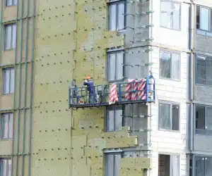 Aislamiento térmico en edificio en construcción, trabajo de instalación en fachadas, construcción de vivienda de alta eficiencia energética, obra de aislamiento exterior, técnicas de construcción sostenibles.