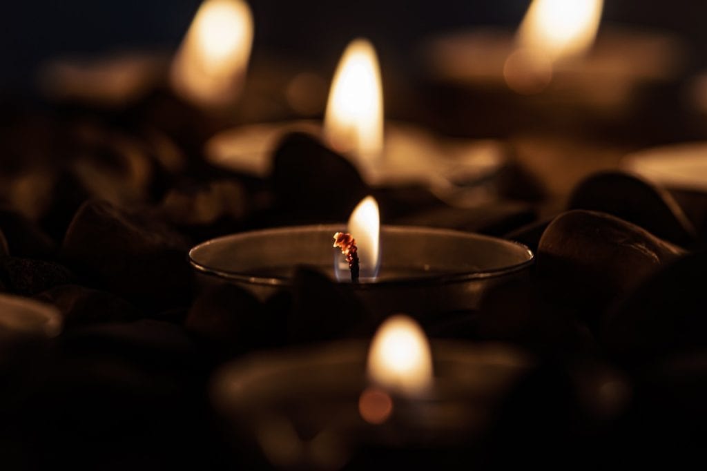 Centros de vela encendidos en la oscuridad, velas en recipientes de vidrio con piedras alrededor, ambiente tranquilo y meditativo, ideal para momentos de reflexión y espiritualidad. – SoyMigrante.com REVISTA