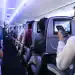 Vuelos internacionales con pantallas de entretenimiento a bordo de avión, pasajeros usando dispositivos móviles, experiencia en viajes, tecnología en aviación, entretenimiento en vuelo, viajeros conectados.