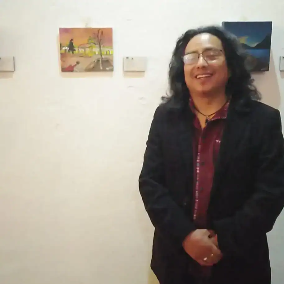 Retrato de un hombre con gafas y cabello largo en una galería de arte, sonriendo. – SoyMigrante.com REVISTA