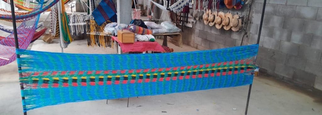 Entretejido artesanal colorido en mercado tradicional mexicano, exhibiendo tejidos y accesorios culturales, representando la riqueza de la cultura indígena en comunidades rurales. – SoyMigrante.com REVISTA