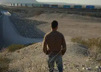 Exilio y migración en frontera México-Estados Unidos, joven observando trenes en tren de carga en el desierto, tema de migrantes centroamericanos en movimiento hacia Estados Unidos, noticias de migración.