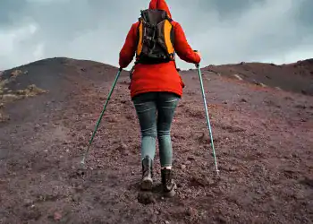 Exploradora caminando en una montaña volcánica con equipo de senderismo, representando aventura y superación.