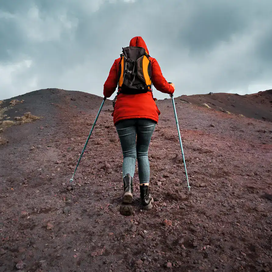 Exploradora caminando en una montaña volcánica con equipo de senderismo, representando aventura y superación. – SoyMigrante.com REVISTA
