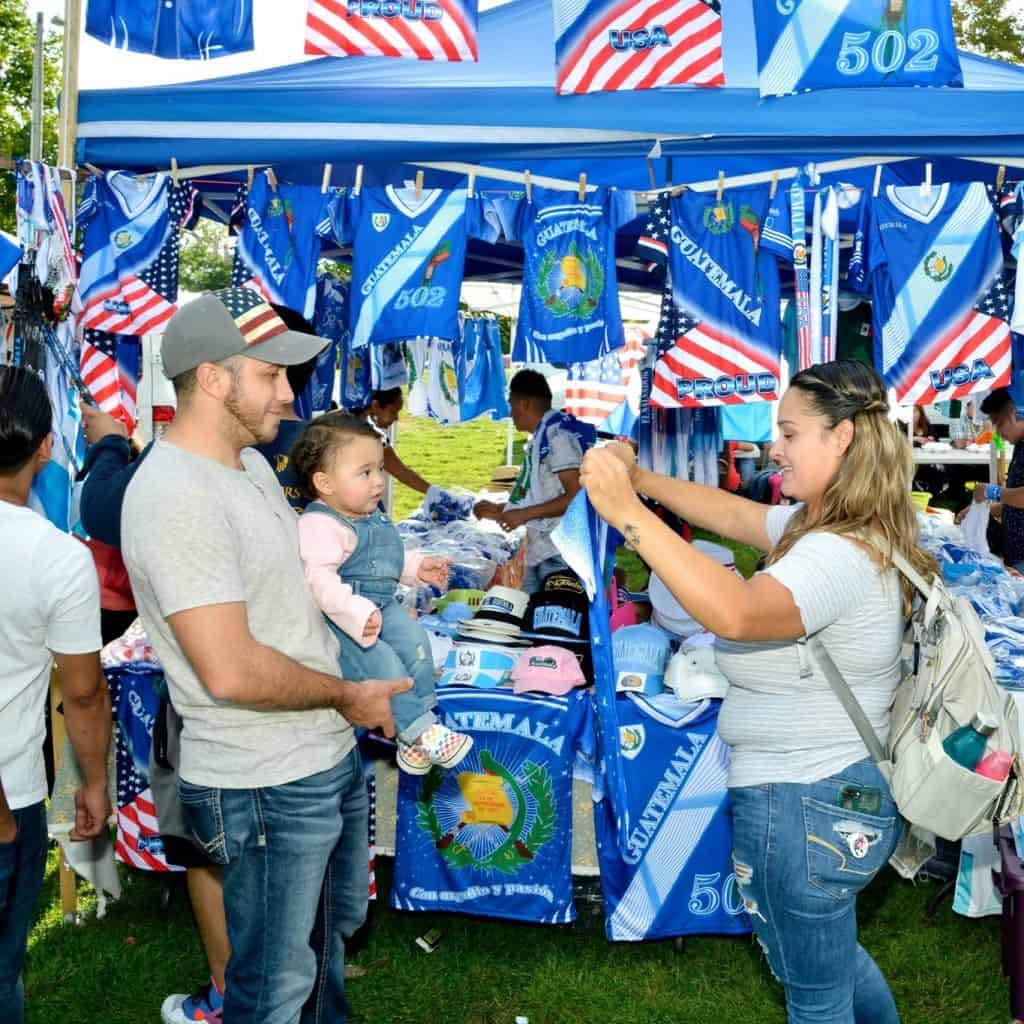 Camisa, bandera y souvenirs de Guatemala en puesto de venta en evento cultural de inmigrantes en EE. UU. – SoyMigrante.com REVISTA