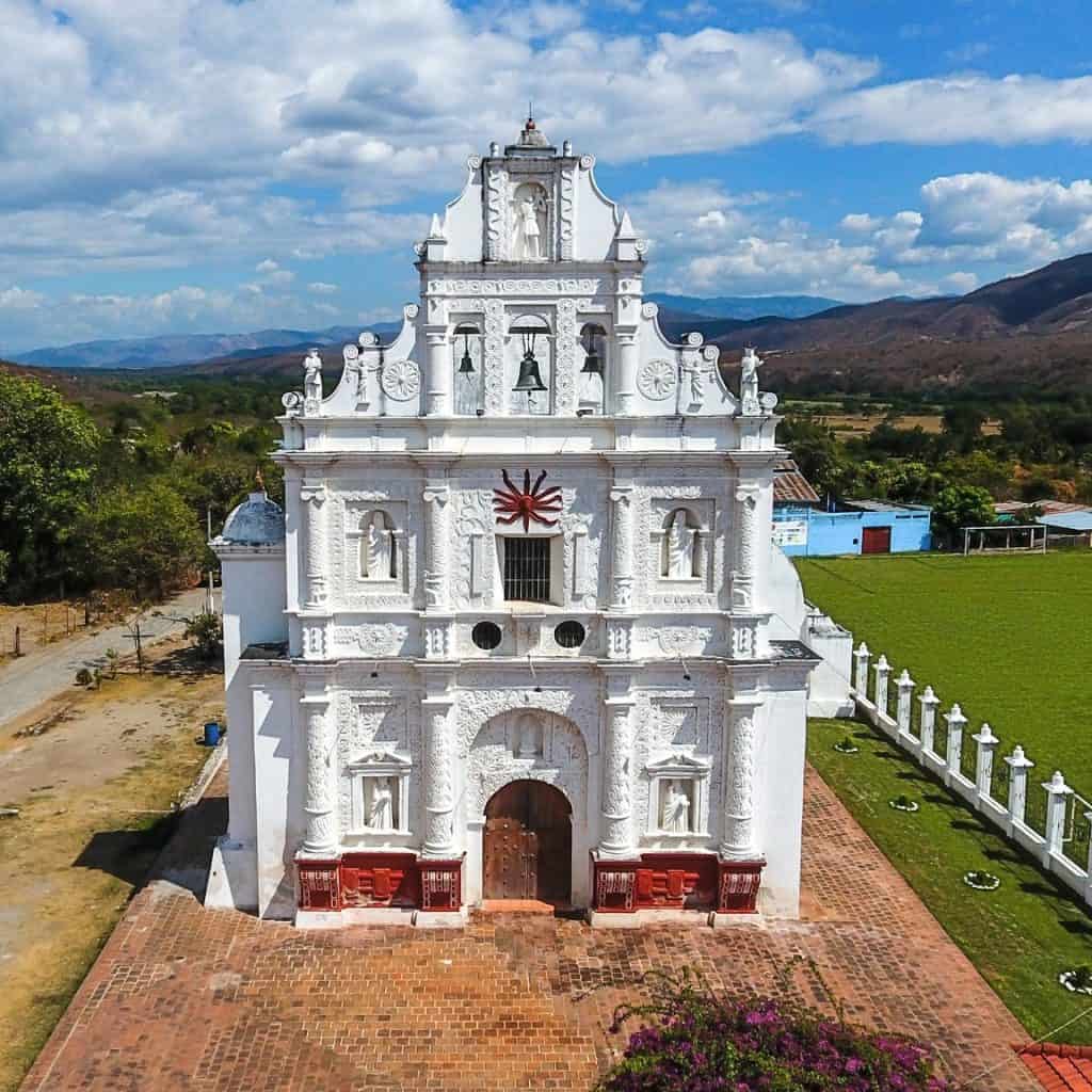 Imágenes de la iglesia colonial en un pueblo de México con paisaje montañoso y cielo despejado, representando patrimonio cultural y arquitectónico. – SoyMigrante.com REVISTA
