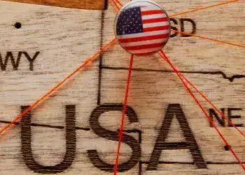 USA flag on the pin with red thread showed the paths on the wooden map – SoyMigrante.com REVISTA America, Estados Unidos, inmigración, comunidad migrante, inmigrantes en EE.UU., derechos de migrantes, integración social, historia migratoria, apoyo a migrantes, cultura inmigrante, revista SoyMigrante.com.