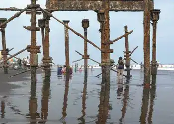 Barco abandonado en la playa con estructura oxidation en el agua, turismo en la costa, paisaje marítimo, deterioro y historia de barcos en la playa, deterioro en estructuras navales, cultura marítima y viajes costeros.