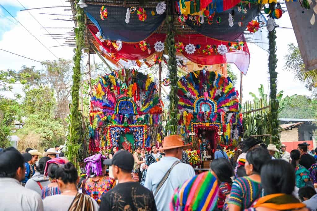 Coloridas decoraciones tradicionales en celebración indígena en Guatemala, con alta participación comunitaria y vestimenta folklórica durante festividad cultural. – SoyMigrante.com REVISTA