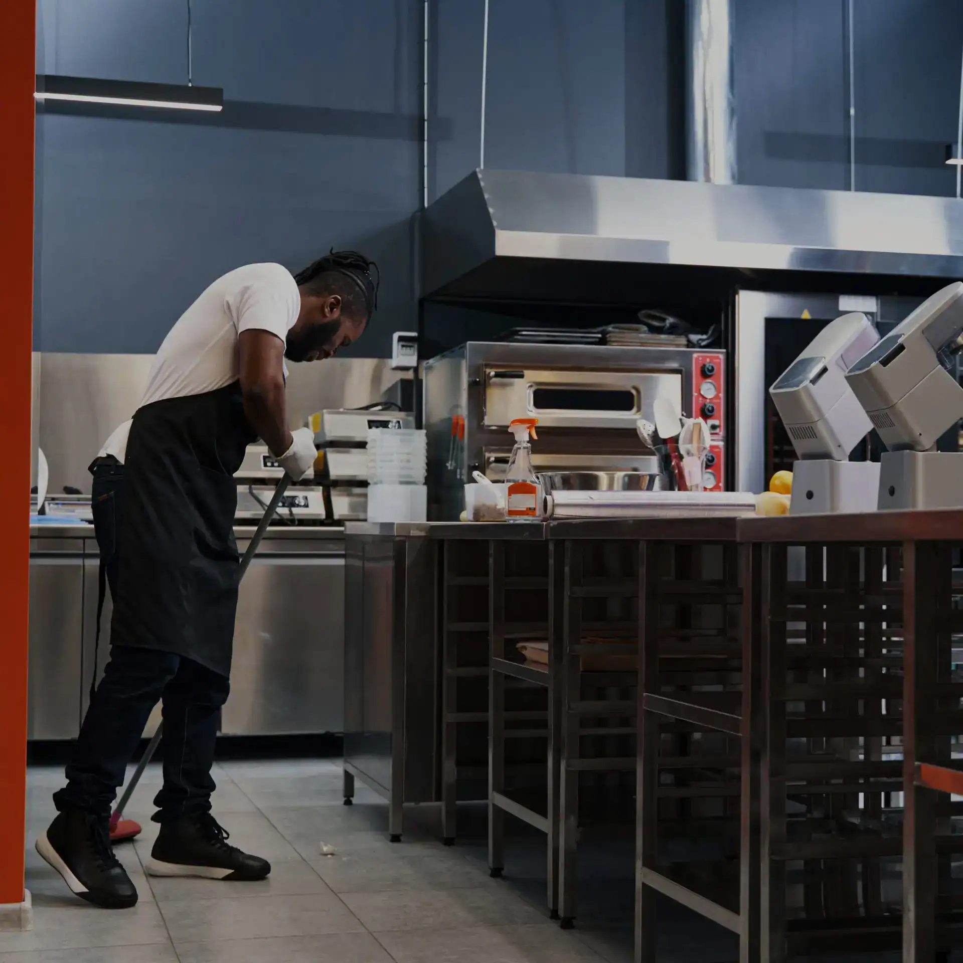 Trabajador de restauración limpiando en cocina profesional, ambiente de gastronomía moderna, enfoque en higiene y trabajo en equipo para la excelencia culinaria.