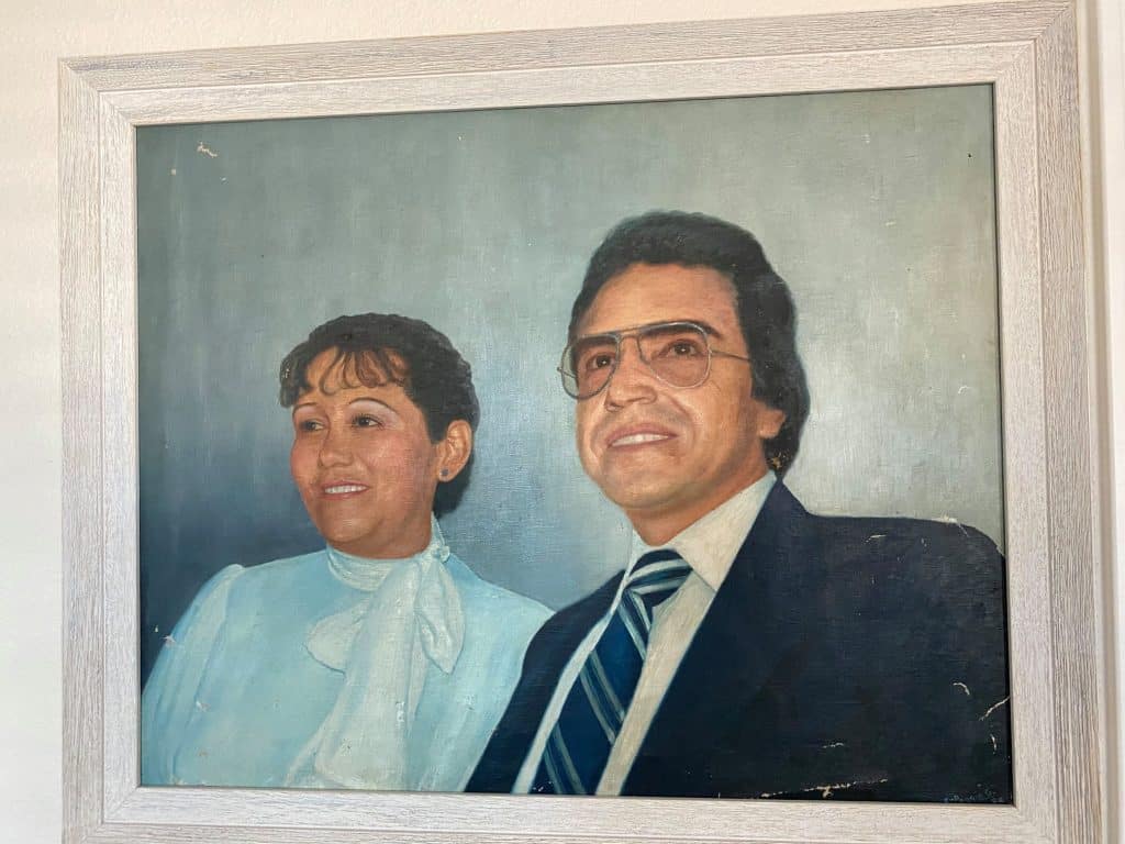 Retrato de un hombre y una mujer, posiblemente de época pasada, vestido formal y con expresión seria en un ambiente de oficina o hogar. – SoyMigrante.com REVISTA