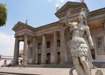 Imponente escultura de una diosa en la entrada del edificio histórico con columnas y detalles clásicos.