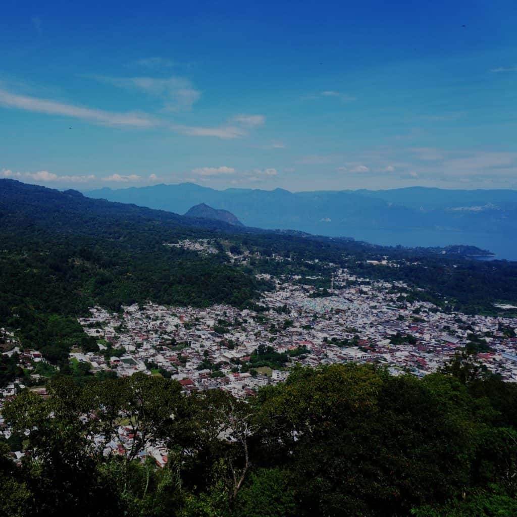 Paisaje de montaña y ciudad en Guatemala, vista panorámica desde una colina con bosque, cielos despejados, ambiente urbano y natural, en un entorno de migración y comunidades rurales. – SoyMigrante.com REVISTA
