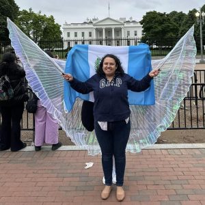 Vendedora con alas de mariposa en protesta frente a la Casa Blanca, representando la comunidad migrante en Estados Unidos. Imagen de activismo y derechos migratorios. – SoyMigrante.com REVISTA