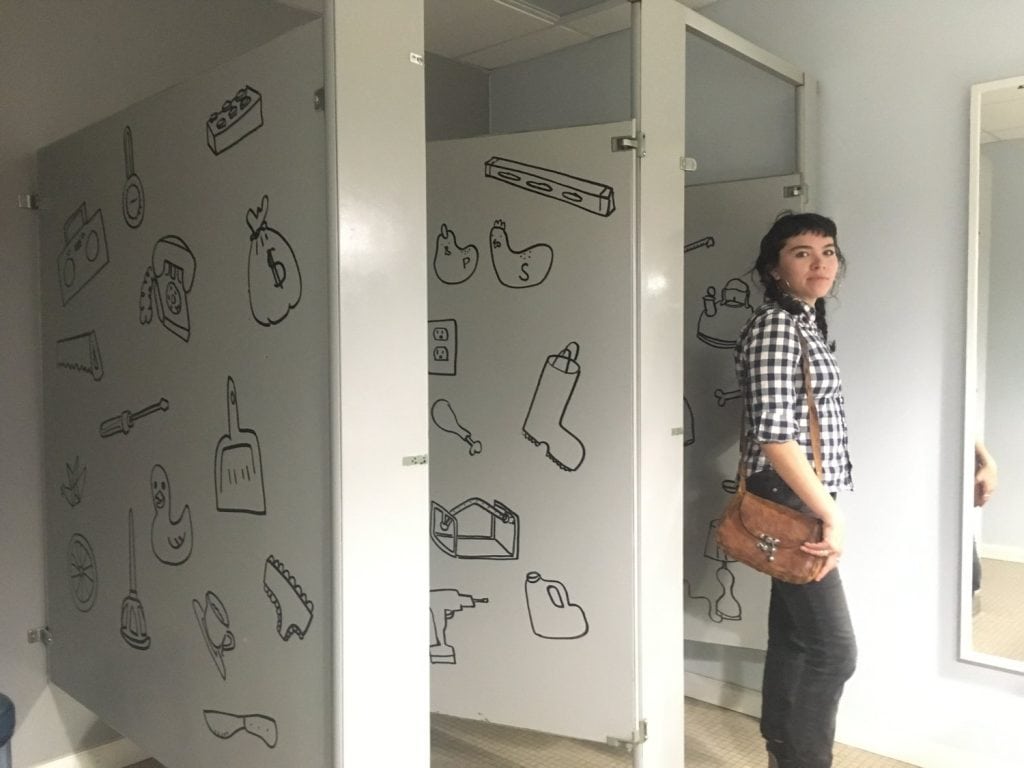 Lavabo en baño público con ilustraciones de herramientas y objetos cotidianos en las paredes.