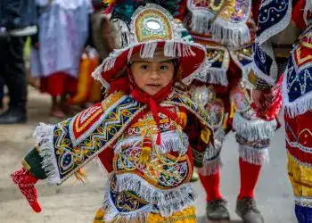 Niña en celebración tradicional con vestimenta colorida y sombrero adornado, participando en una fiesta cultural en México.