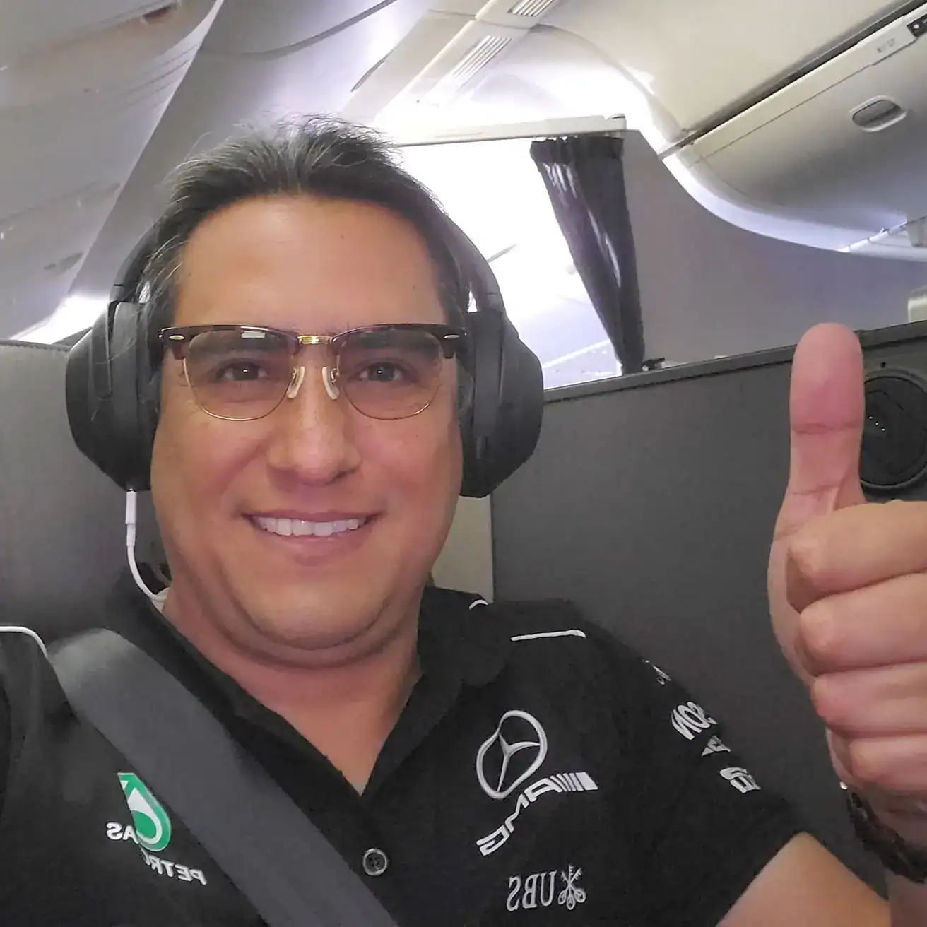 Vinicio Villatoro migrante guatemalteco en Texas, donde es consultor de negocios para empresas de USA, Europa y Asia. empezó su vida en usa como valet parking – SoyMigrante.com REVISTA Rostro de un hombre sonriendo en avión, usando audífonos grandes y camiseta de automóviles, símbolo de satisfacción y confianza en un contexto de viaje y aventura.