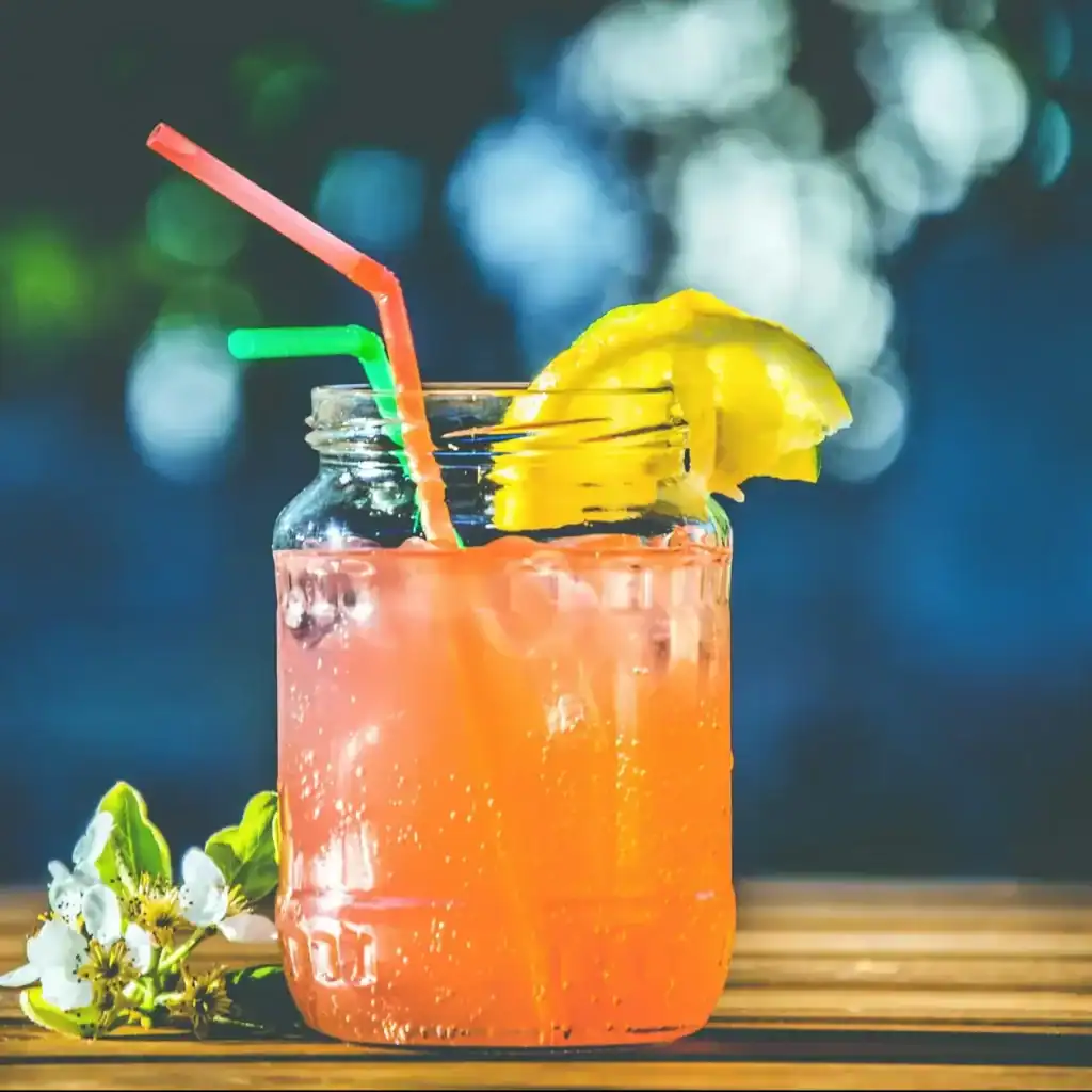 Refresco tropical en tarro con limón y popotes de colores, fondo desenfocado con luz natural, cultura mexicana, bebidas refrescantes, verano, estilo de vida saludable. – SoyMigrante.com REVISTA