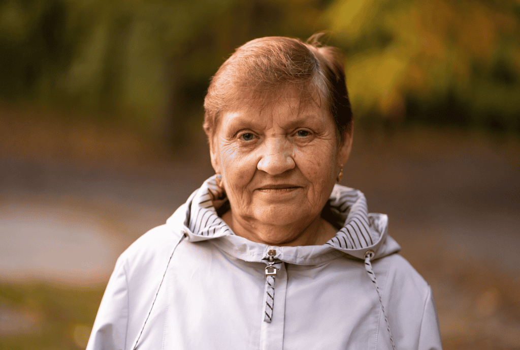 Anciana migrante sonriendo al aire libre, ejemplo de resistencia y fortaleza migratoria en la comunidad latina. – SoyMigrante.com REVISTA