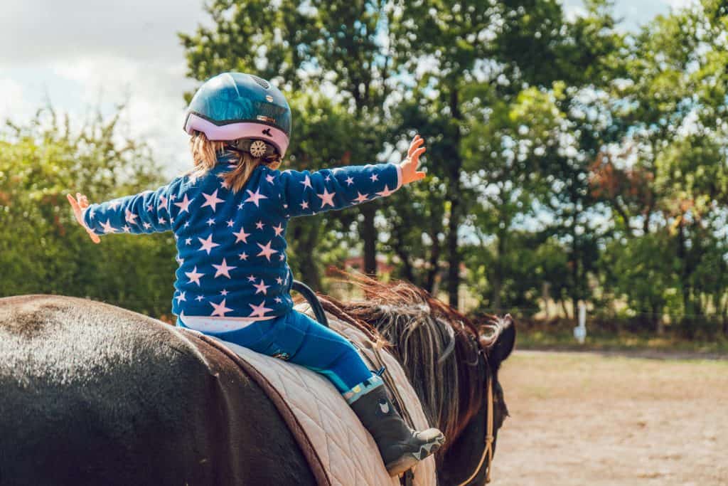 Niña montando a caballo, disfrutando de paseo al aire libre, símbolo de cultura y tradiciones en la revista SoyMigrante.com REVISTA.