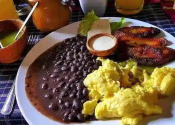 Huevos revueltos, plátanos fritos, frijoles negros y pollo a la parrilla en un desayuno tradicional latinoamericano.