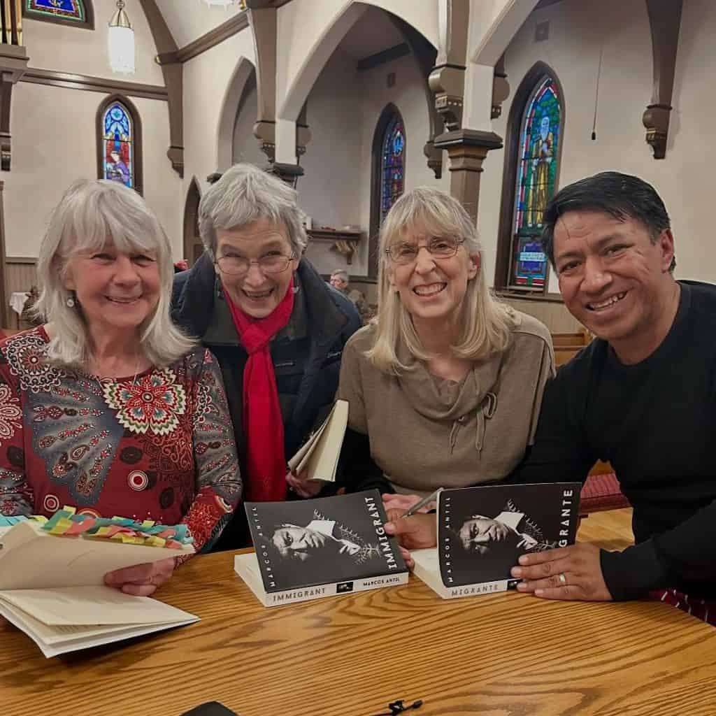 Autoras y autores en una lectura de la revista SoyMigrante.com REVISTA en una iglesia con vitrales coloridos al fondo. – SoyMigrante.com REVISTA