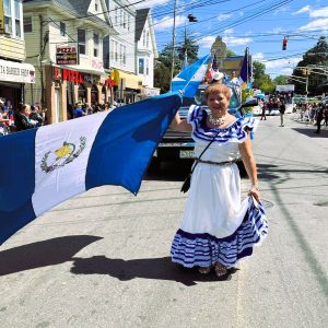 Guatemalteca celebrando en desfile con bandera nacional y traje tradicional, manifestación cultural y orgullo de Guatemala en evento festive del país.